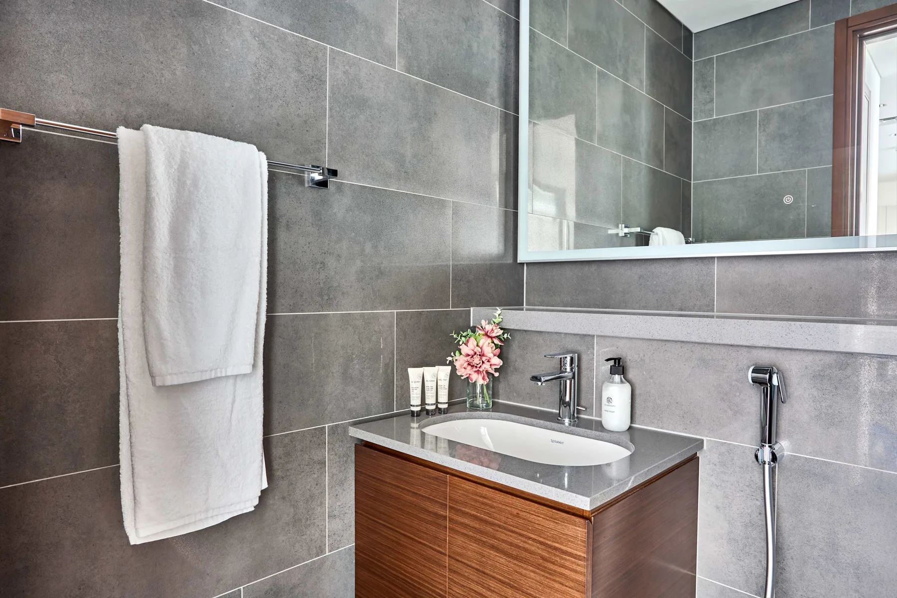 Un tocador de baño moderno con lavabo, espejo y paredes de azulejos grises.