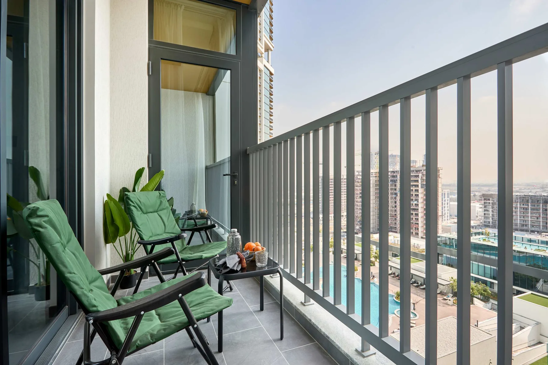 Una zona de estar en un balcón ofrece vistas a edificios y una piscina.