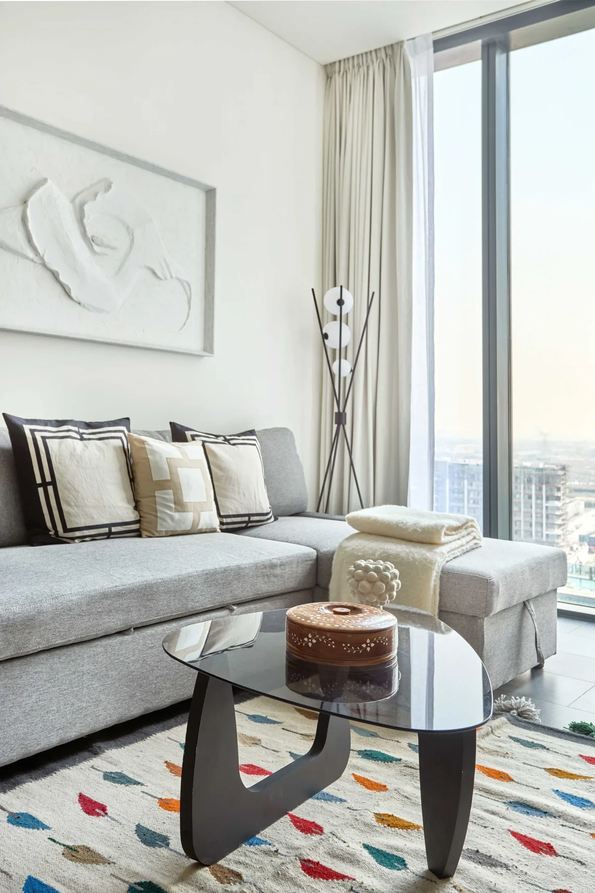 Una sala luminosa con un sofá seccional gris y una mesa de centro de vidrio.
