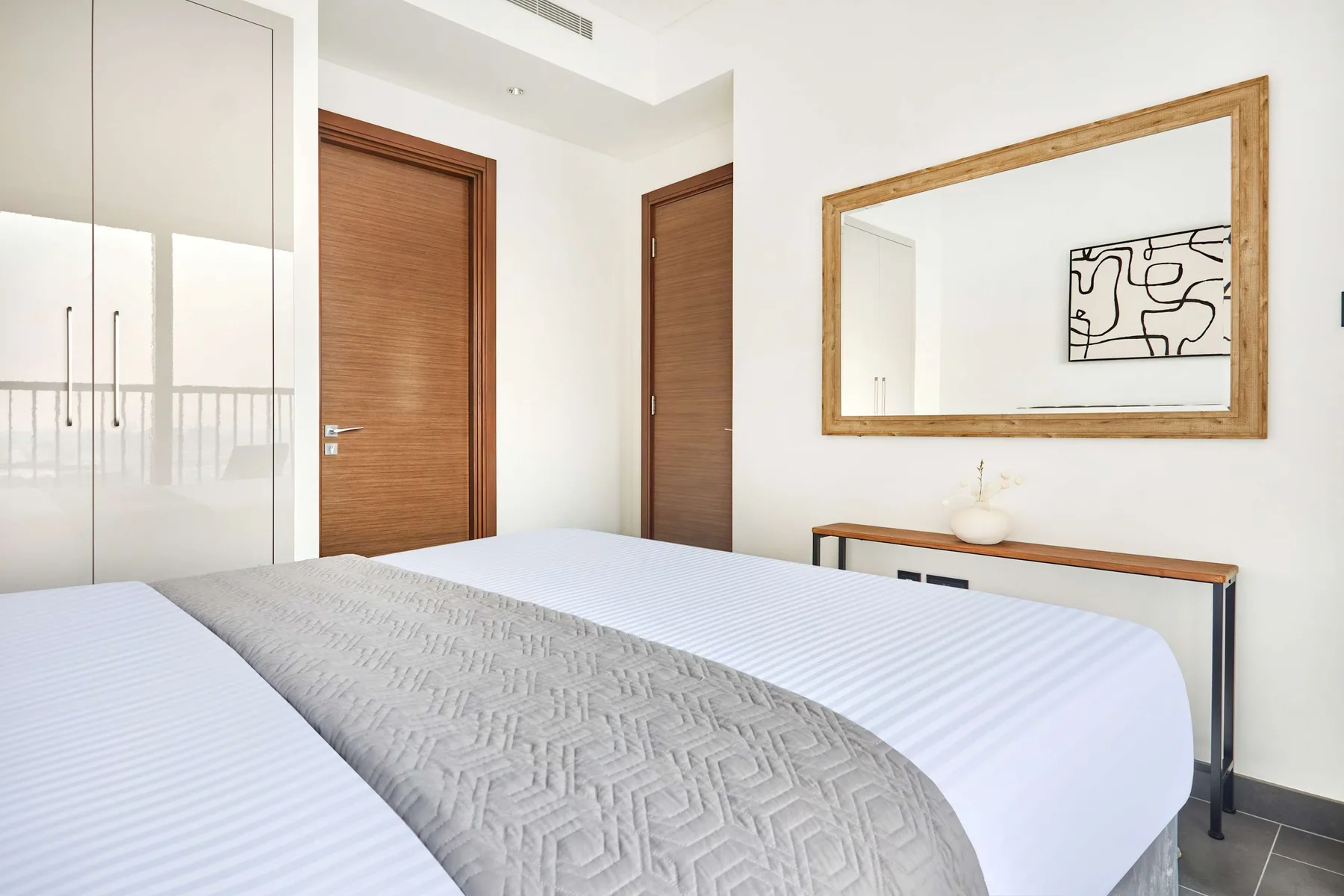 Un dormitorio luminoso con una cama bien tendida y un espejo grande en la pared.