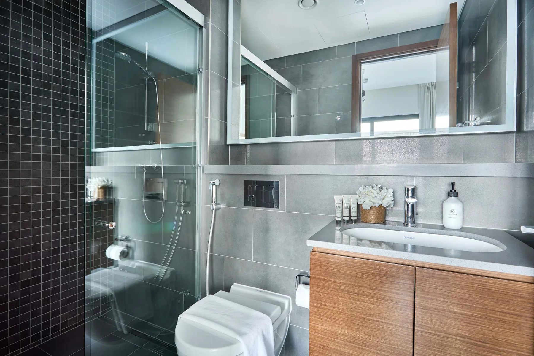 Un baño moderno con ducha de vidrio, inodoro y tocador de madera.