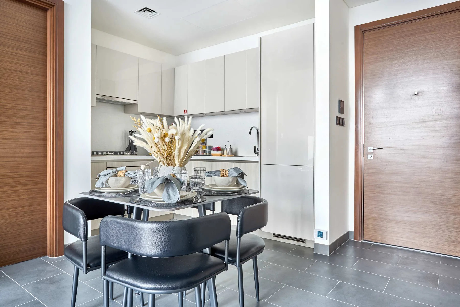 Una mesa de comedor con asientos oscuros está en una cocina luminosa.