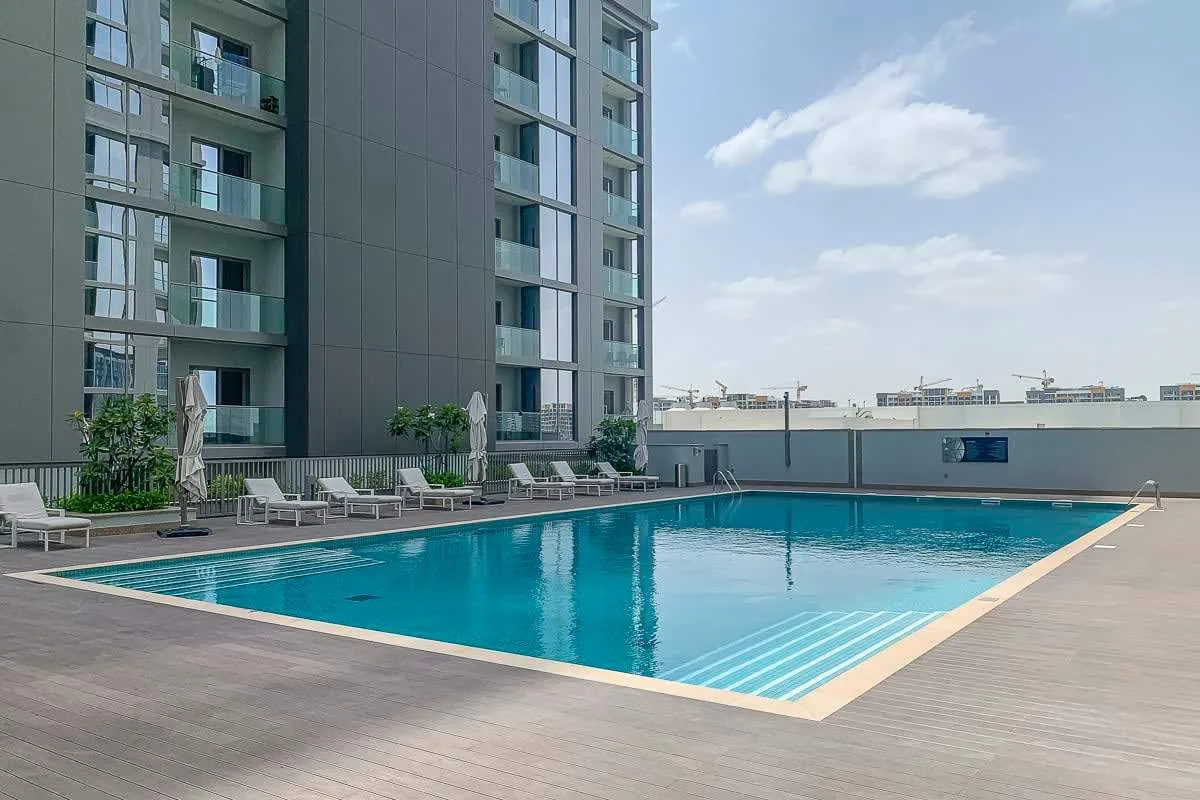 Una piscina junto a un edificio moderno, con asientos de descanso alrededor.