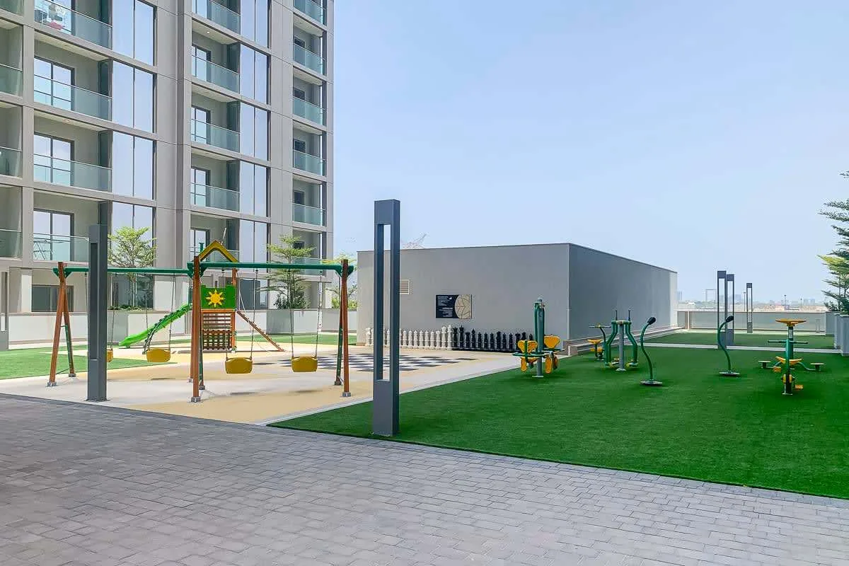 Zona exterior de juegos y ejercicio con césped artificial junto a un edificio de apartamentos.