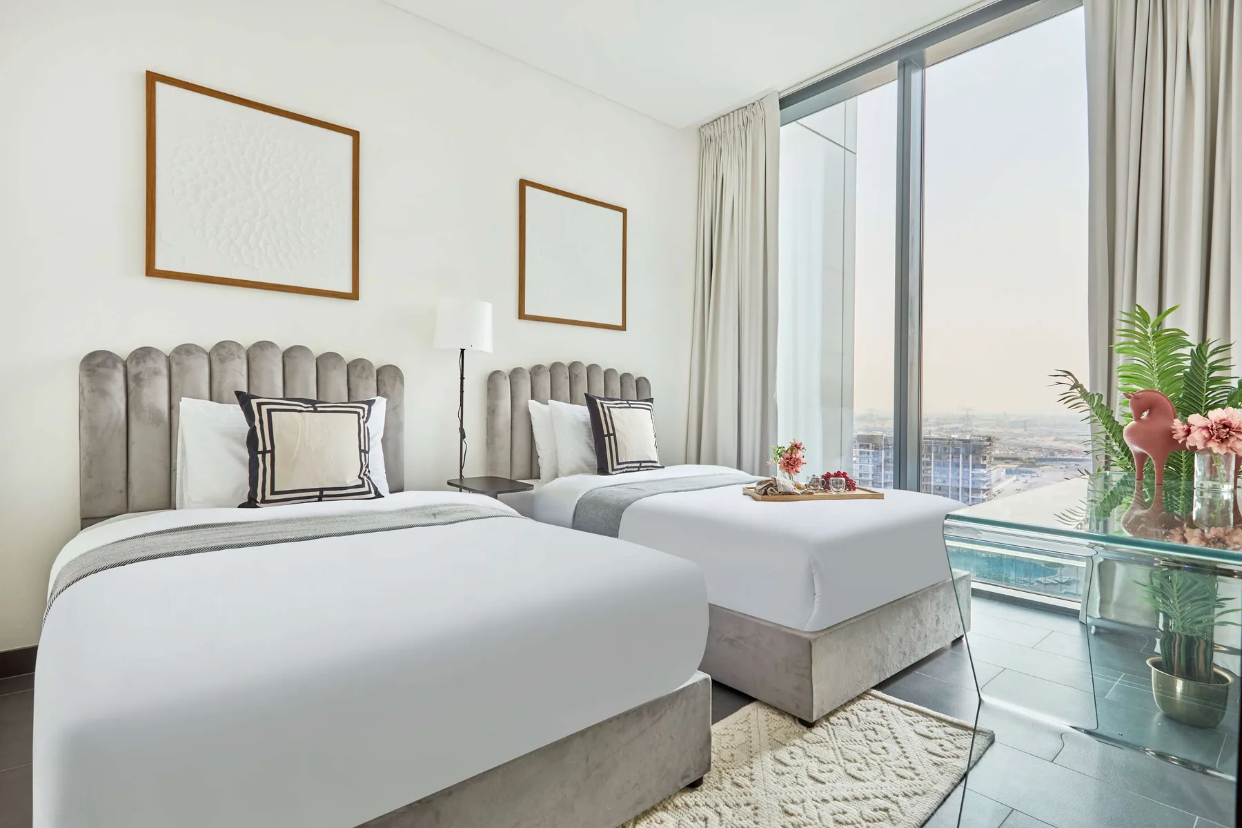 Un dormitorio luminoso con dos camas junto a ventanales de piso a techo.