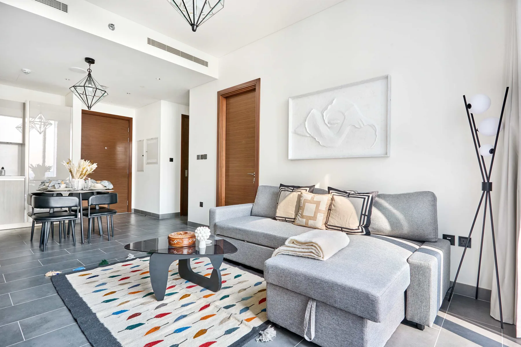 Una sala luminosa con asientos grises, una alfombra estampada y un comedor.