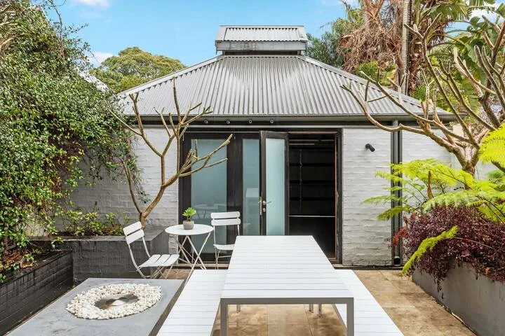 Un patio exterior pavimentado con una mesa larga, asientos y una puerta corrediza de vidrio.