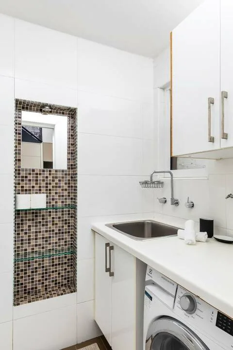 Un baño alicatado con lavabo y una lavadora de carga frontal.