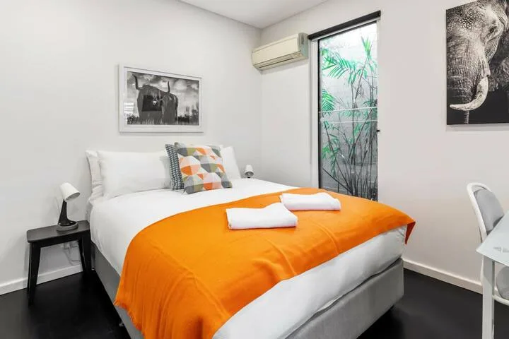Dormitorio con una cama cubierta por una manta naranja junto a una ventana.