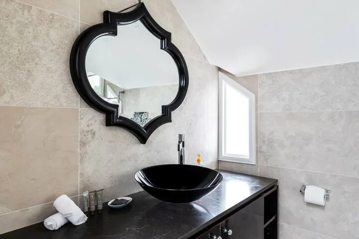 Un tocador de baño con lavabo negro sobre la encimera, espejo y ventana.