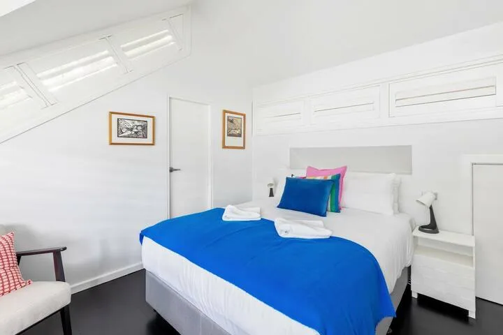 Un dormitorio luminoso con una cama cubierta por una manta azul y cojines de colores.