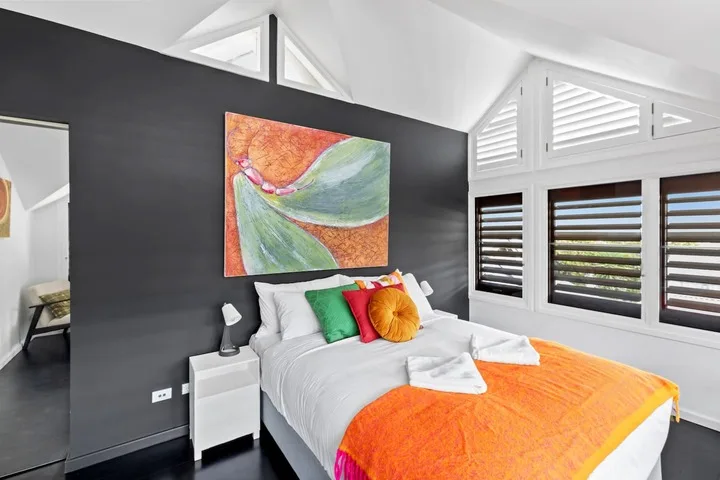 Dormitorio con una cama vestida de blanco y ropa de cama naranja brillante.