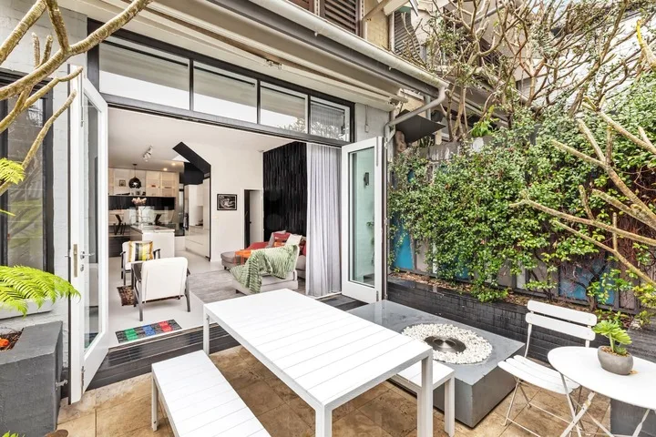 Un comedor en el patio se abre a una sala de estar, con un jardín frondoso a un lado.