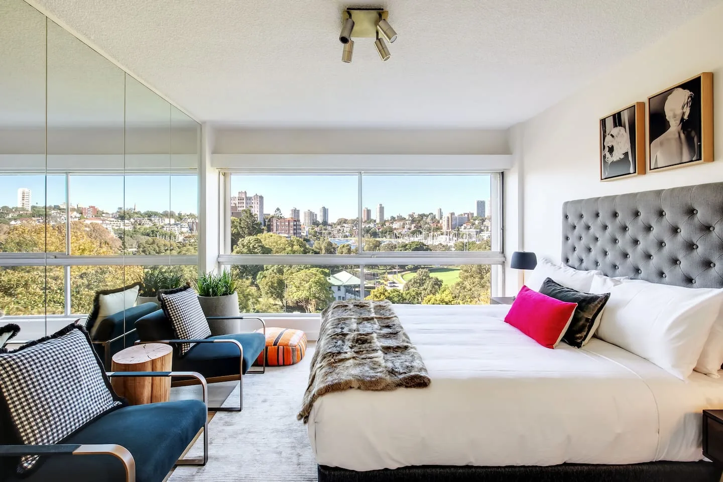 Un dormitorio con una cama grande, asientos y amplias ventanas con vistas a la ciudad.