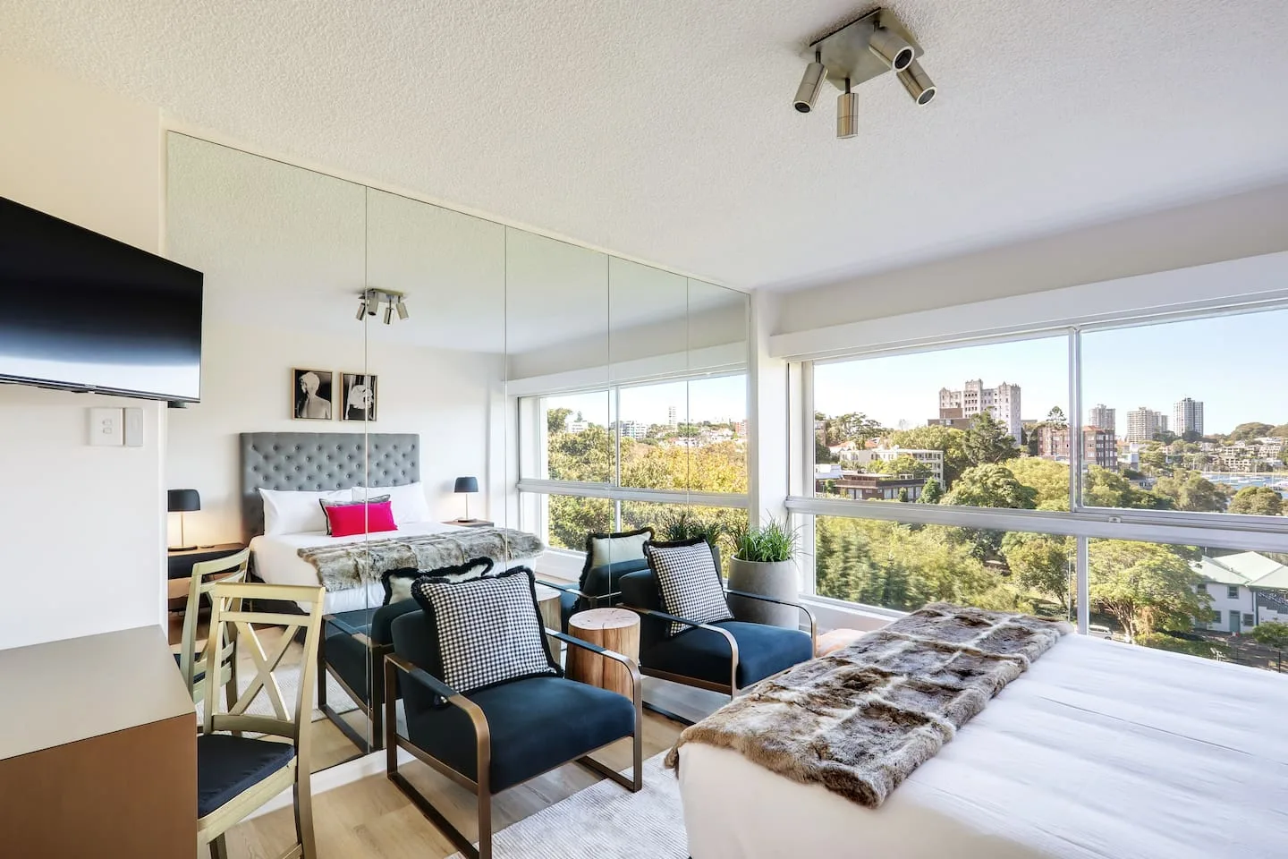 Un dormitorio luminoso con cama, zona de estar y grandes ventanas con vistas a la ciudad.