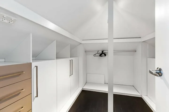 Un área de armario blanca con gabinetes empotrados y espacio para colgar ropa.
