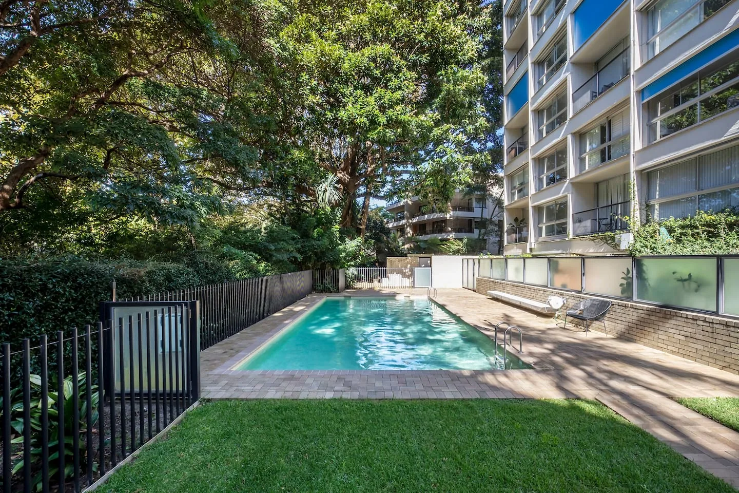Piscina al aire libre junto a un césped y un edificio de varias plantas.