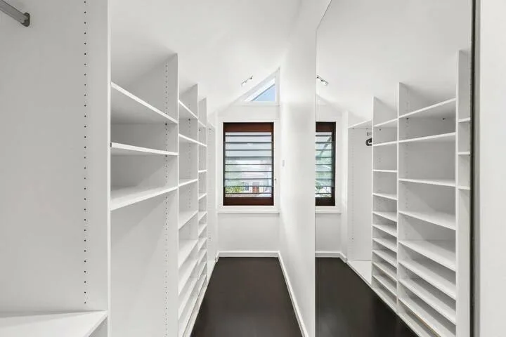 Un vestidor luminoso con estanterías blancas y una ventana.