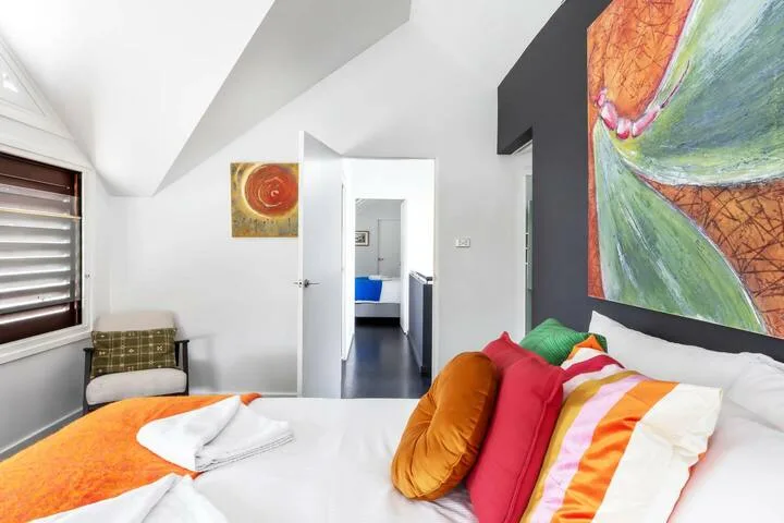 Dormitorio con una cama, cojines coloridos y un gran cuadro abstracto.
