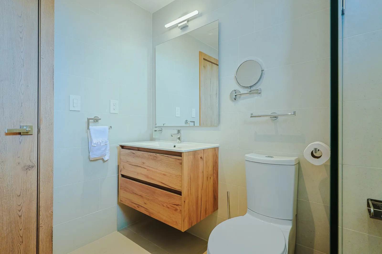 Freshen up in your modern bathroom, featuring a sleek floating vanity, soft lighting, and thoughtful touches like a magnifying mirror—designed for your comfort.