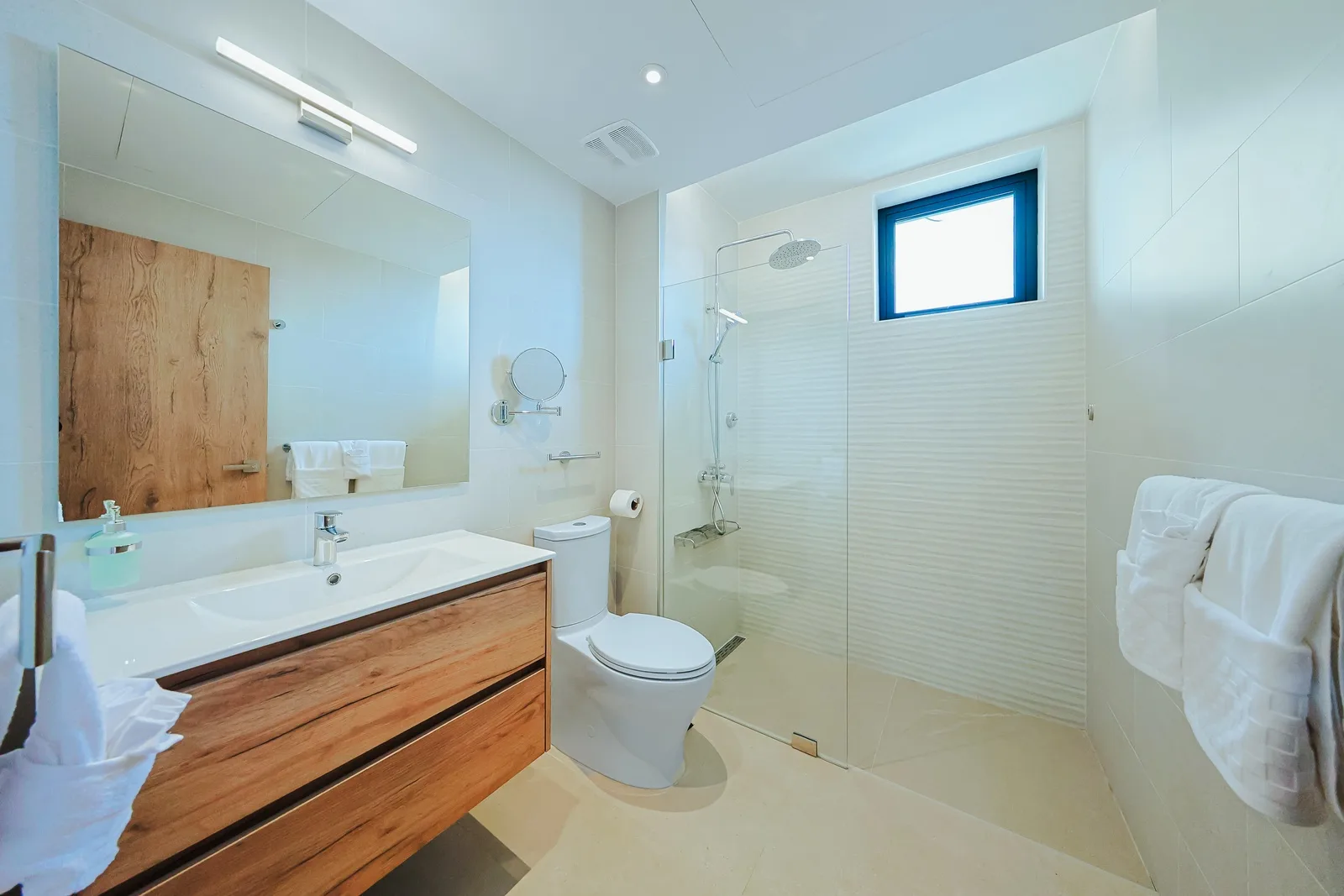 Your private bathroom features a spacious walk-in shower, sleek wood-accented vanity, and soft natural light—designed with modern comfort and style in mind.