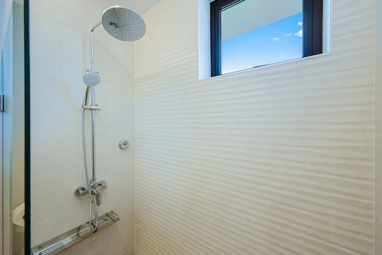 Step into your modern shower with dual heads and textured wave tile—perfect for refreshing after a day of exploration. Natural light streams in, adding warmth to your private retreat.