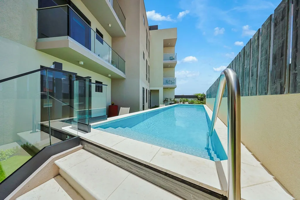 The modern apartment building with glass-railed balconies and a pristine lap pool stretching through the sunny courtyard.