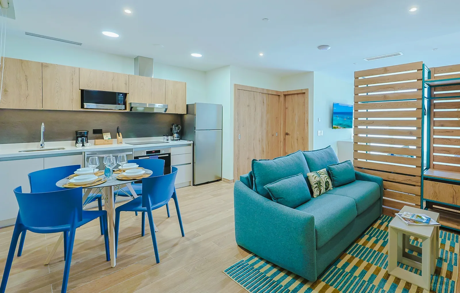 Your bright, modern living space invites relaxation with a plush turquoise sofa, fully equipped kitchen, and cheerful dining area—perfect for cozy meals and unwinding after exploring the area.