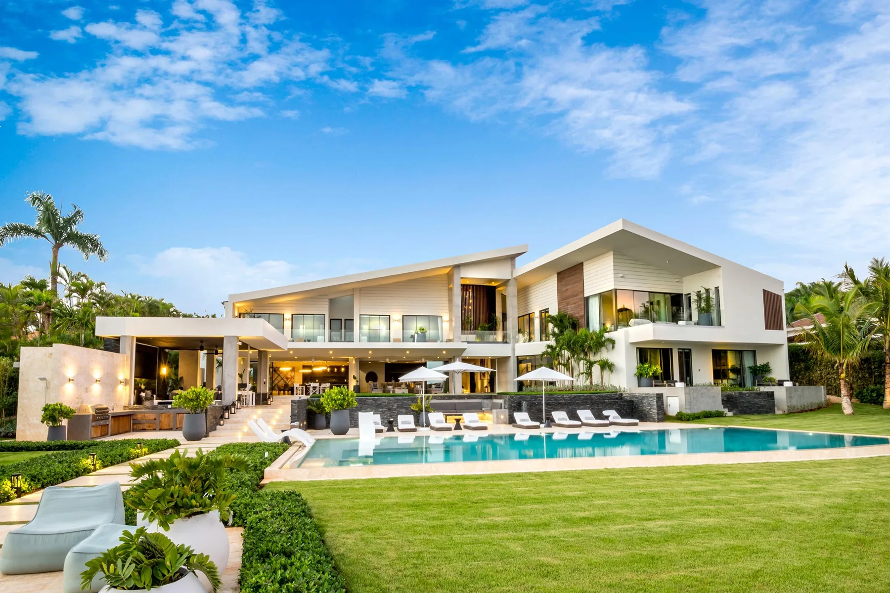 A modern villa stands behind a swimming pool and landscaped lawn.