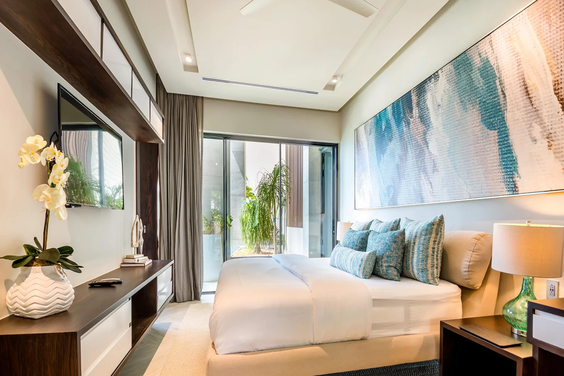 A bright bedroom with a bed, colorful wall art, and glass doors.
