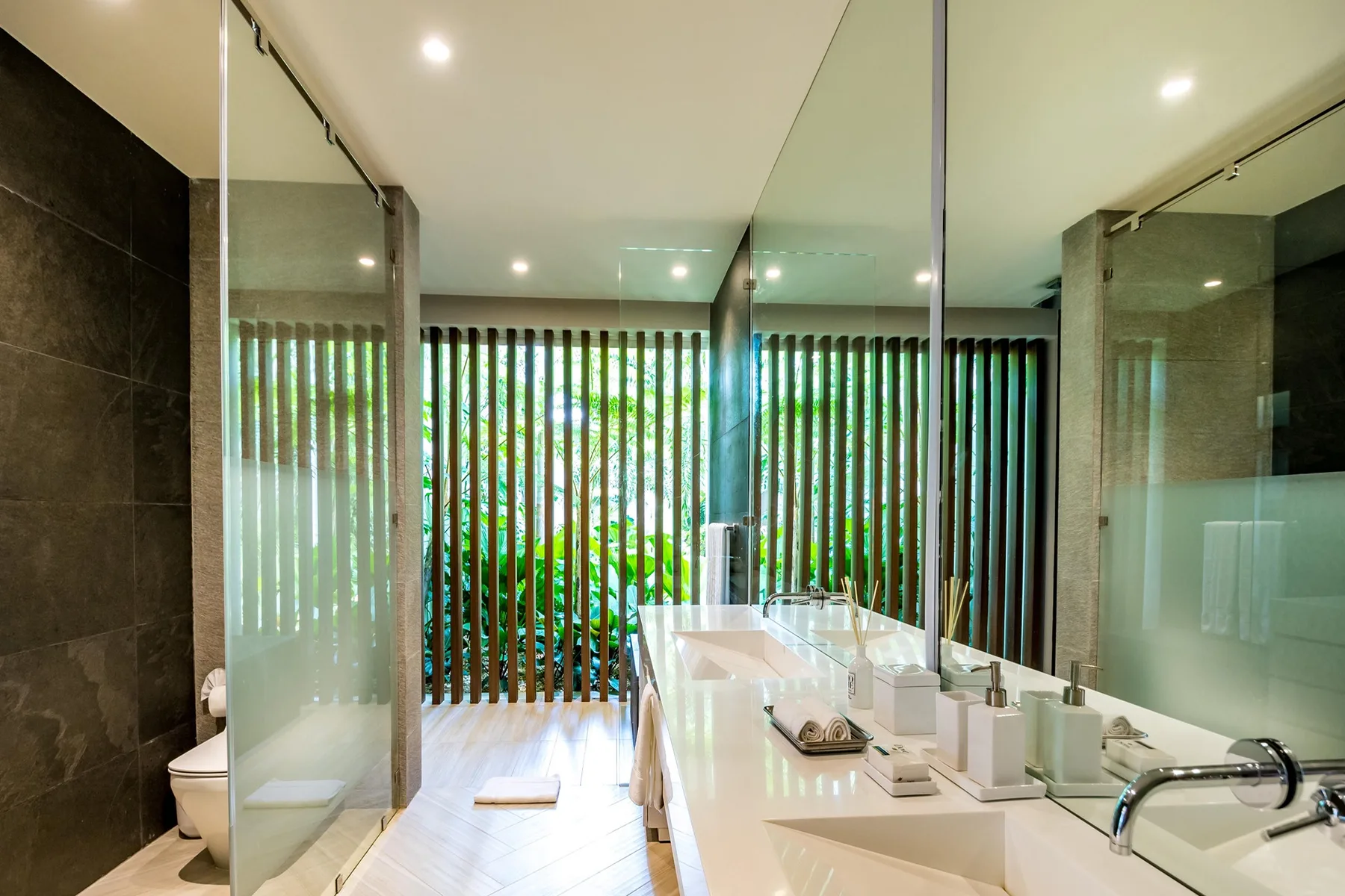 A bright bathroom with a long vanity and vertical slatted screens.