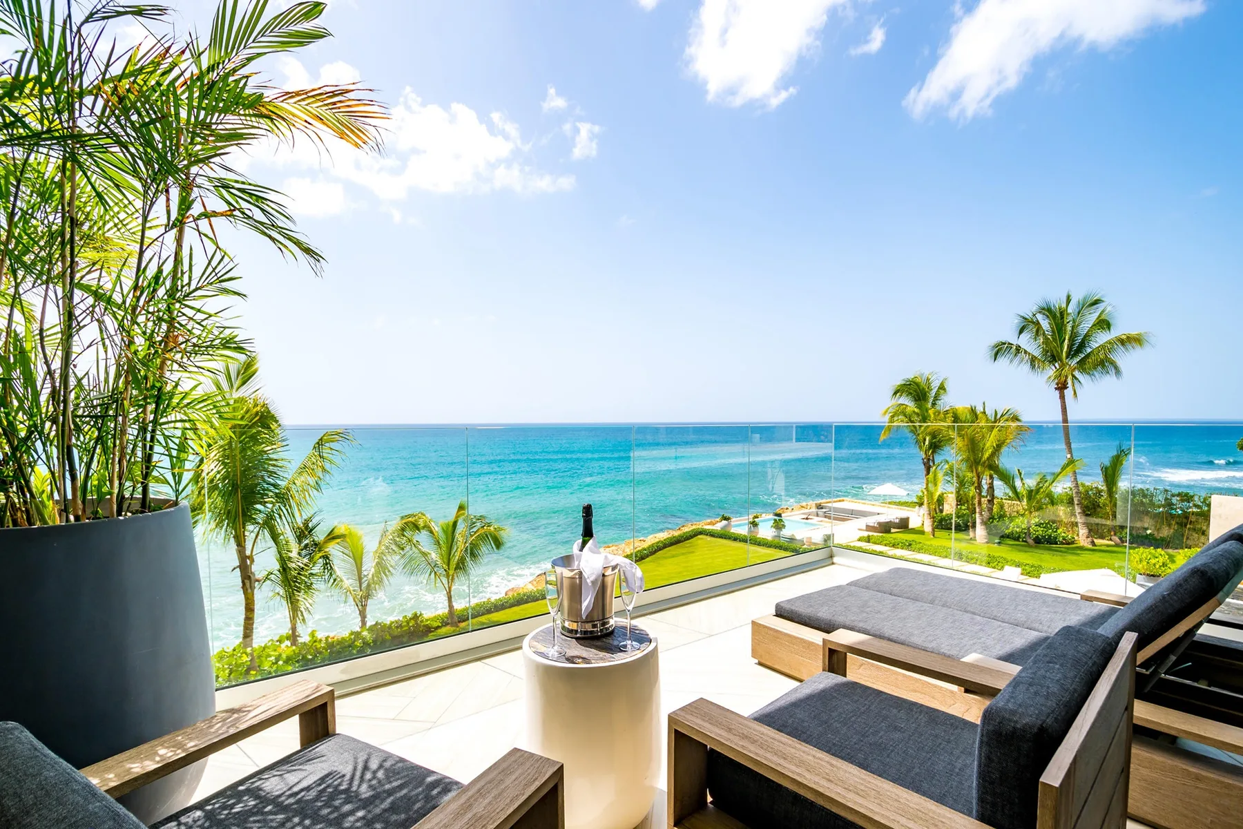 An outdoor lounge overlooks the ocean, with cushioned seating and palm trees.
