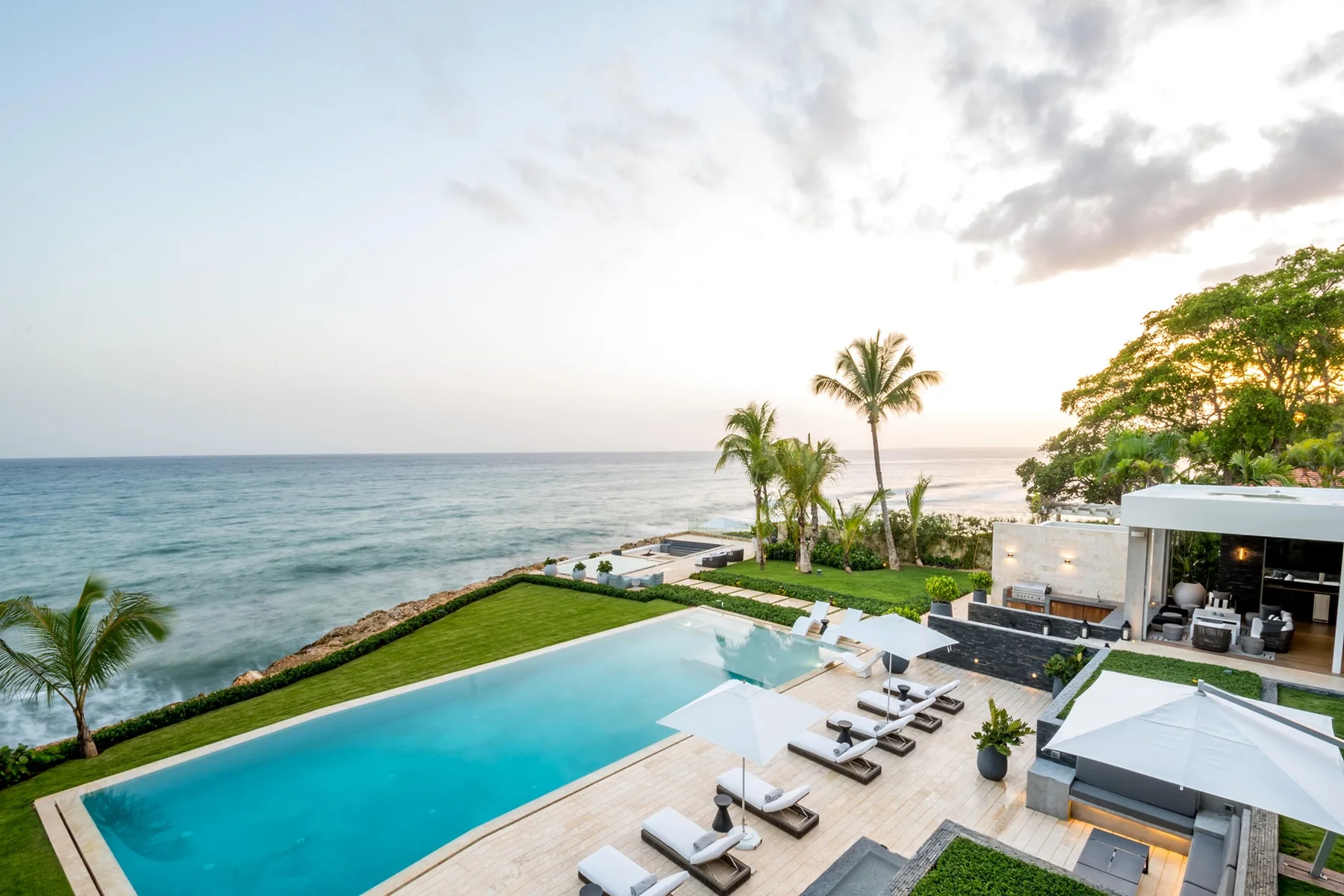 A seaside pool terrace with lounge seating and palm trees.