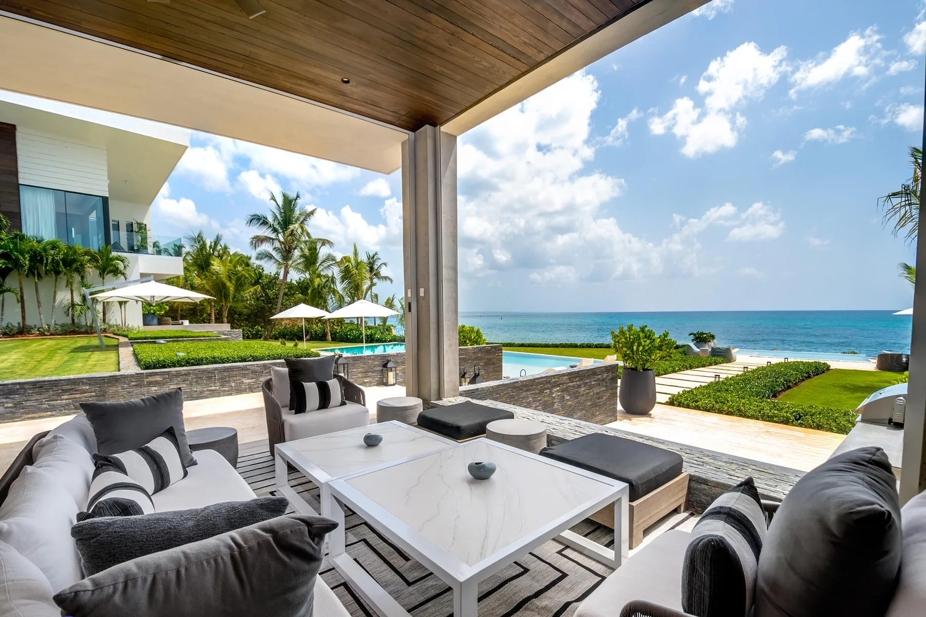 A covered outdoor lounge overlooks a pool and the ocean.