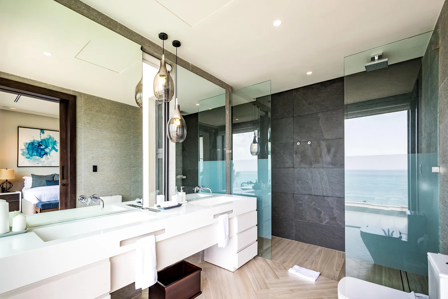 A bright bathroom with a long vanity, glass shower, and ocean views.