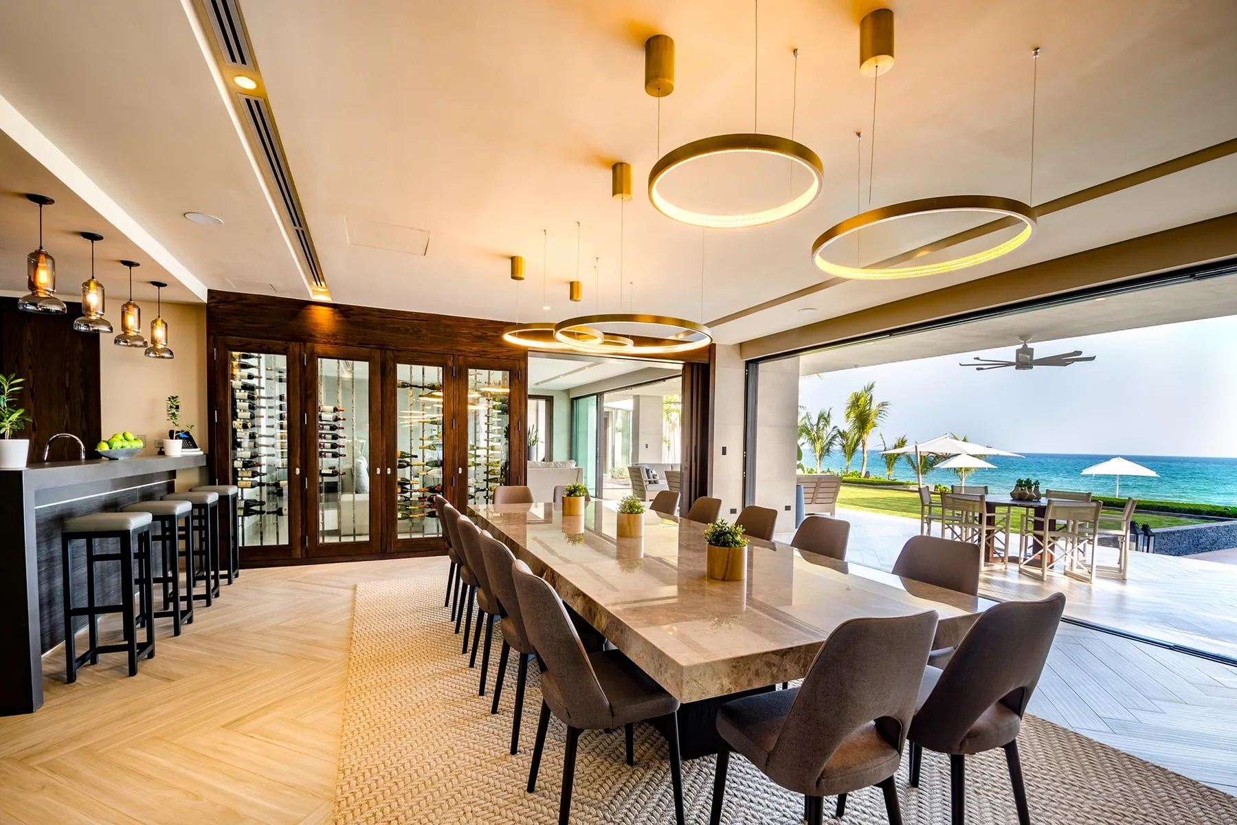 Comedor abierto con una mesa larga junto a la cocina y un patio con vista al mar.