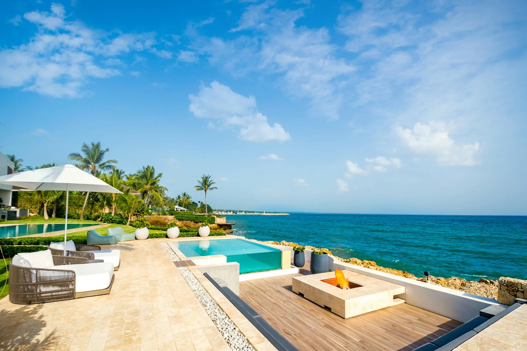 A seaside patio with a pool, outdoor seating, and a built-in fire feature.