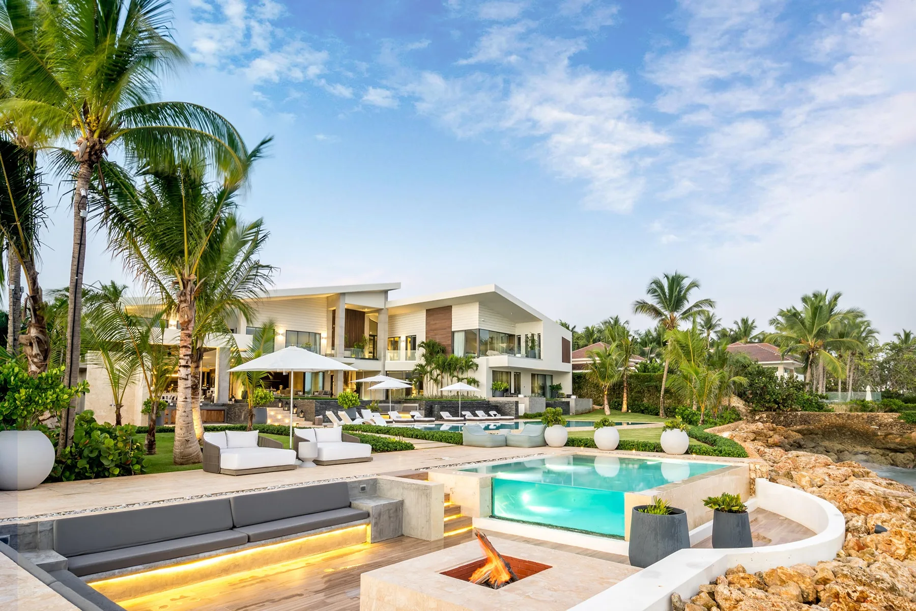 A modern resort-style building overlooks a turquoise pool and landscaped outdoor seating.