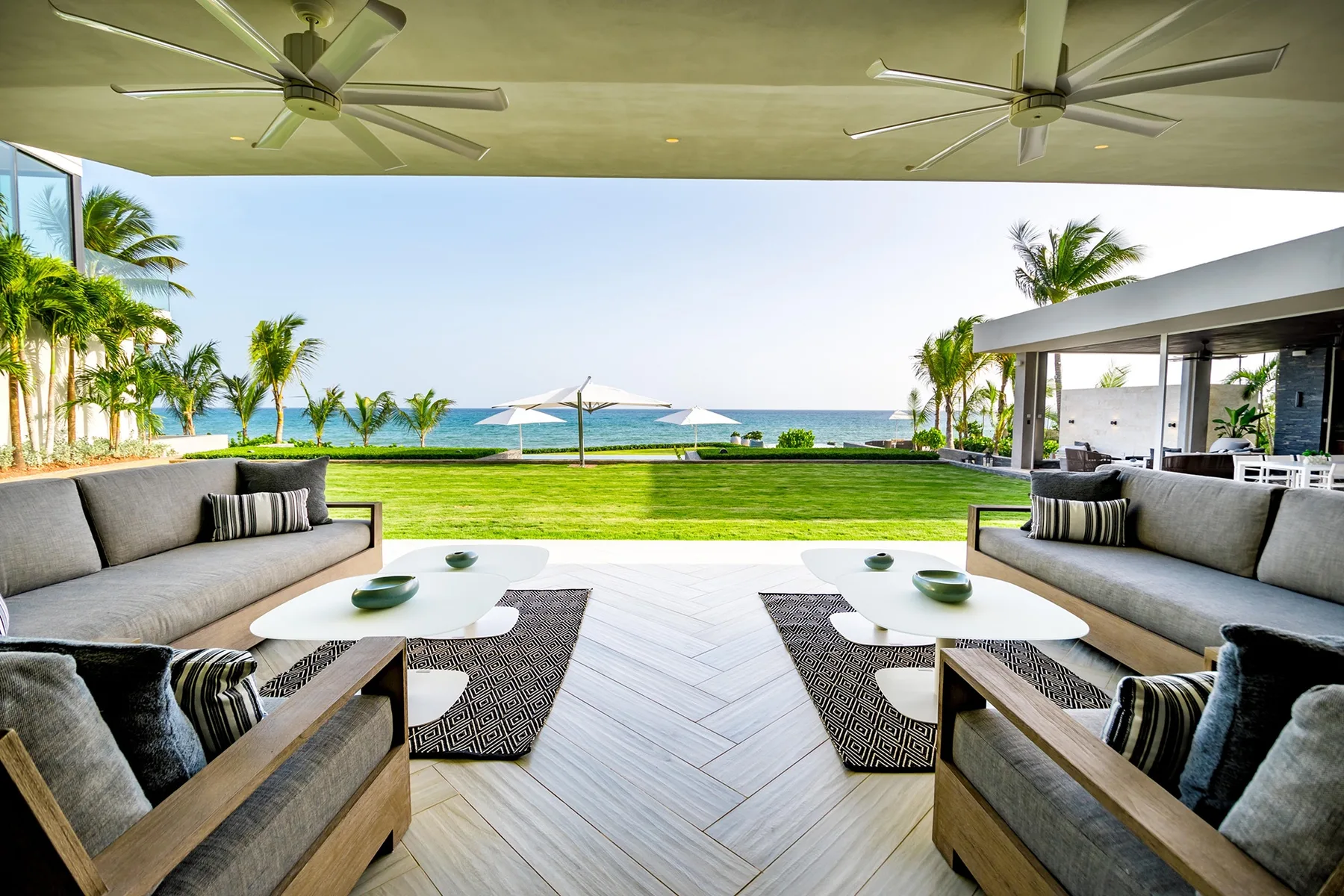 A covered outdoor lounge opens onto a lawn and ocean view.