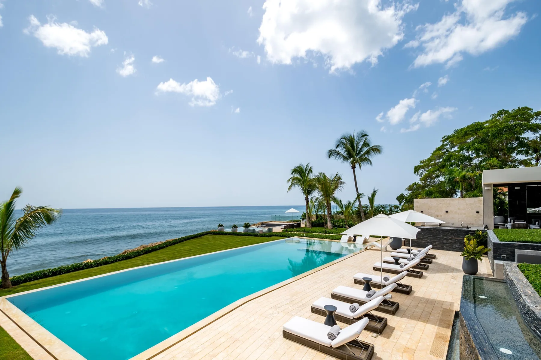 An outdoor swimming pool beside the ocean, with lounge seating along the deck.