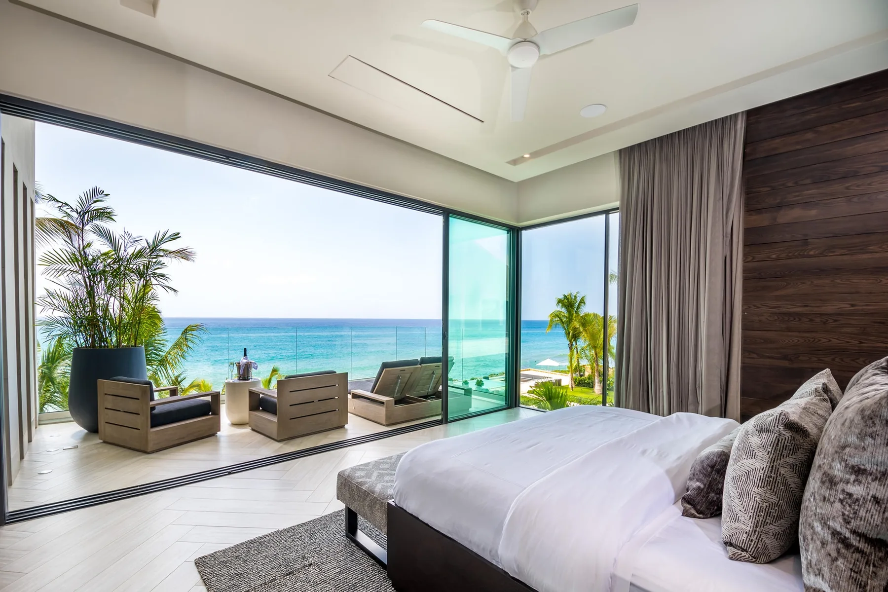 A bedroom opens onto a sea view through large glass windows.