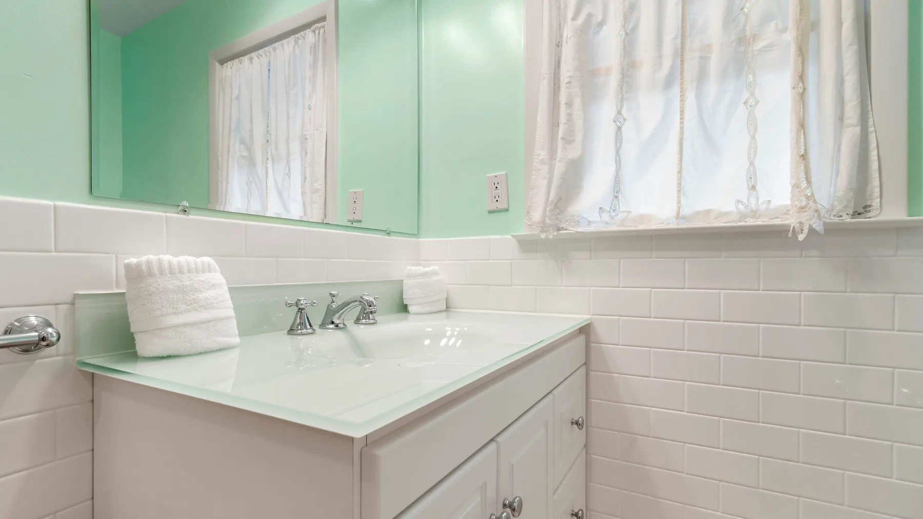 Un tocador de baño con lavabo está bajo una ventana con cortinas.
