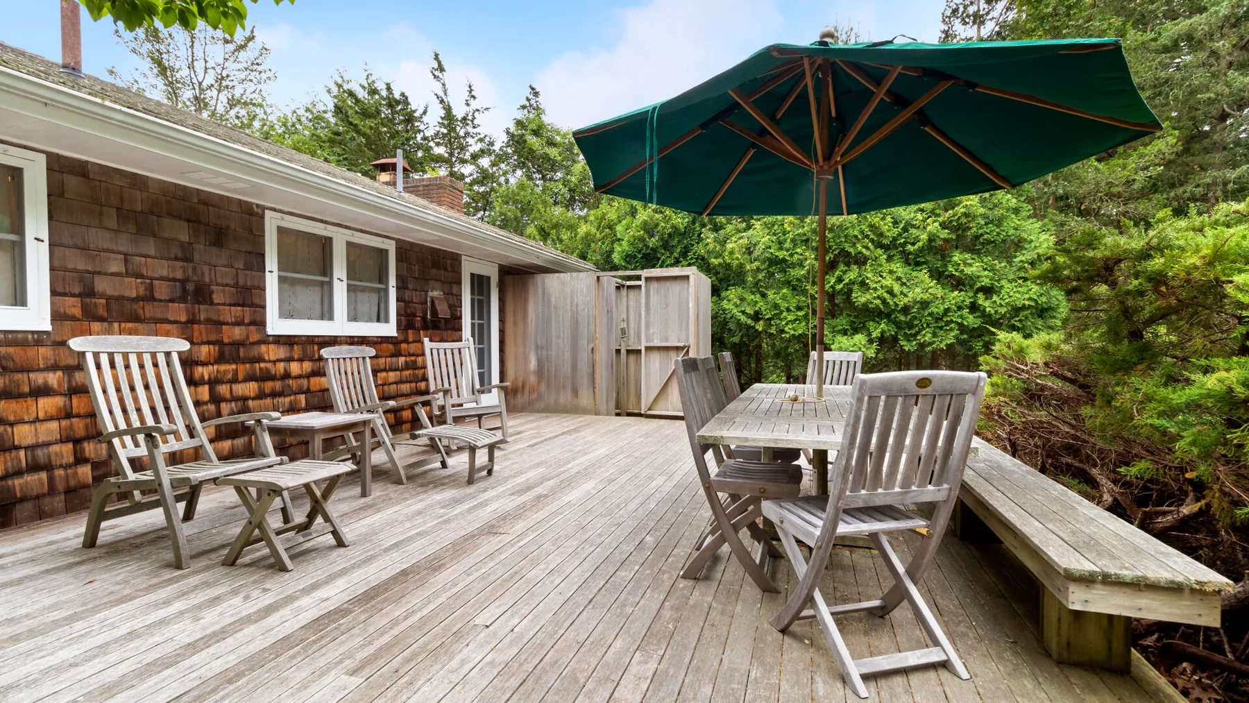 A wooden outdoor deck has a table and seating beneath a large umbrella.