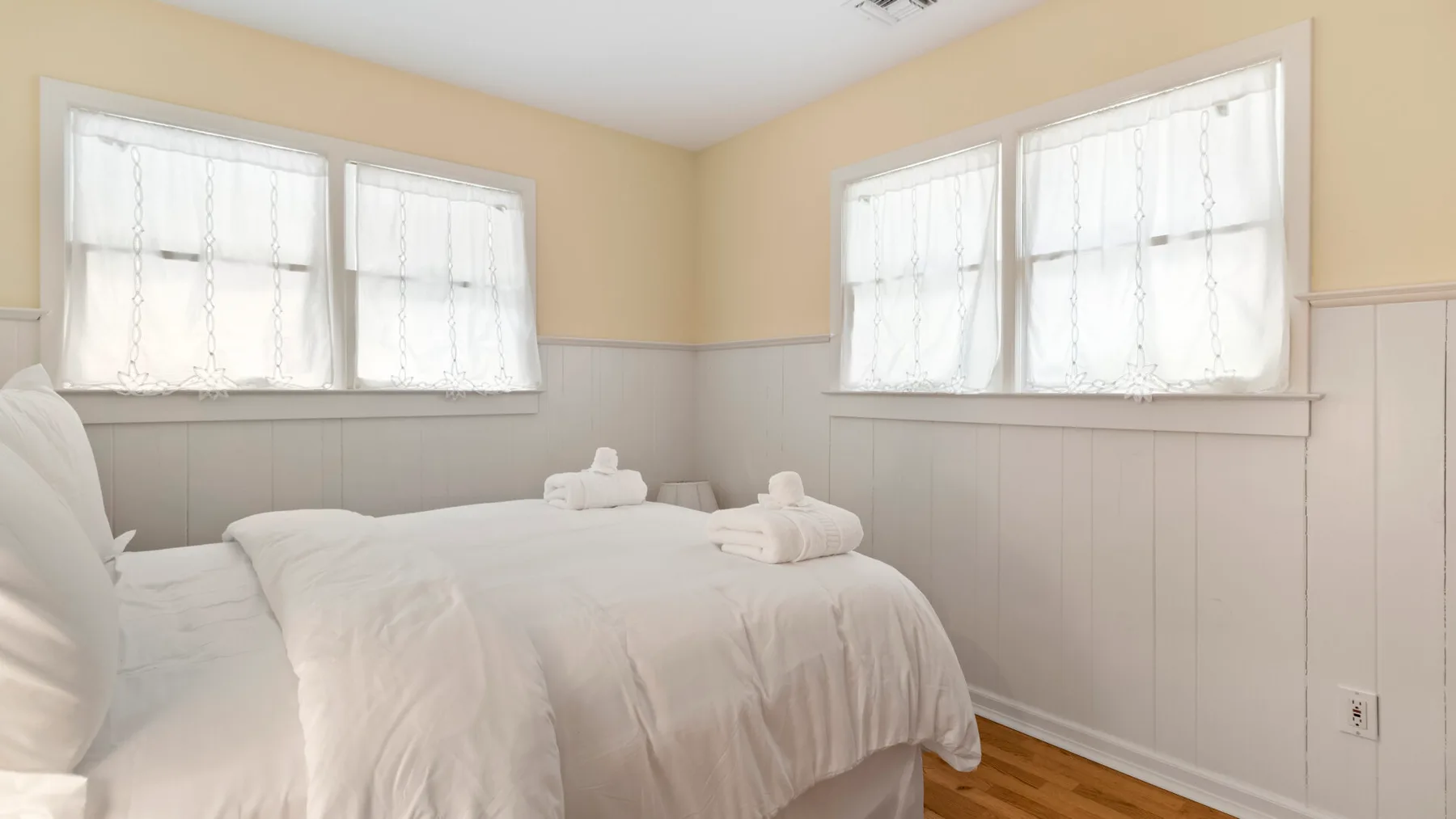 Un dormitorio con ropa de cama blanca y ventanas luminosas.