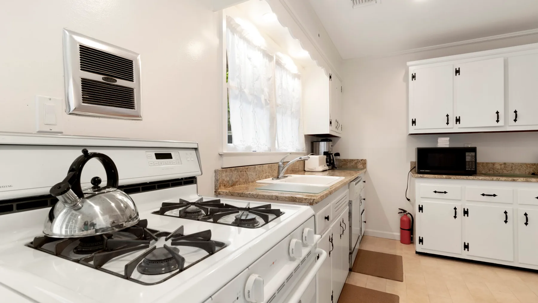 Una cocina luminosa con una estufa de gas, encimera y gabinetes blancos.
