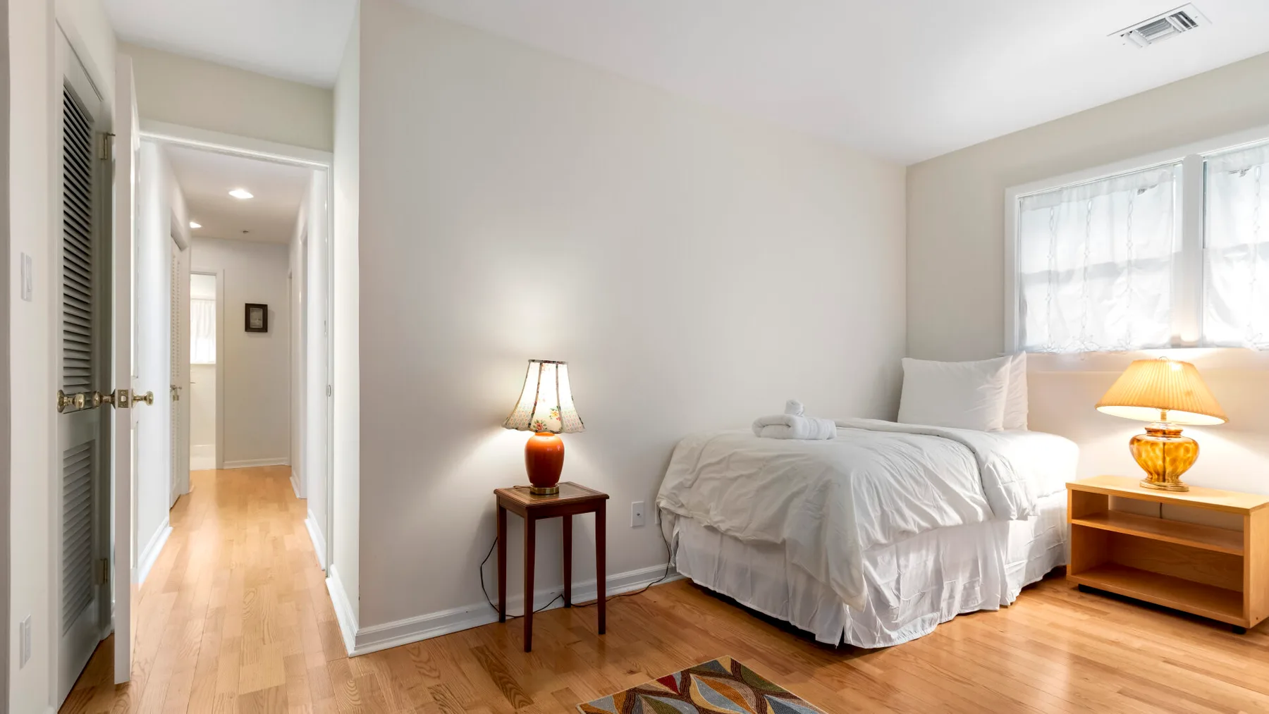 Un dormitorio luminoso con una cama, mesas auxiliares y una ventana.