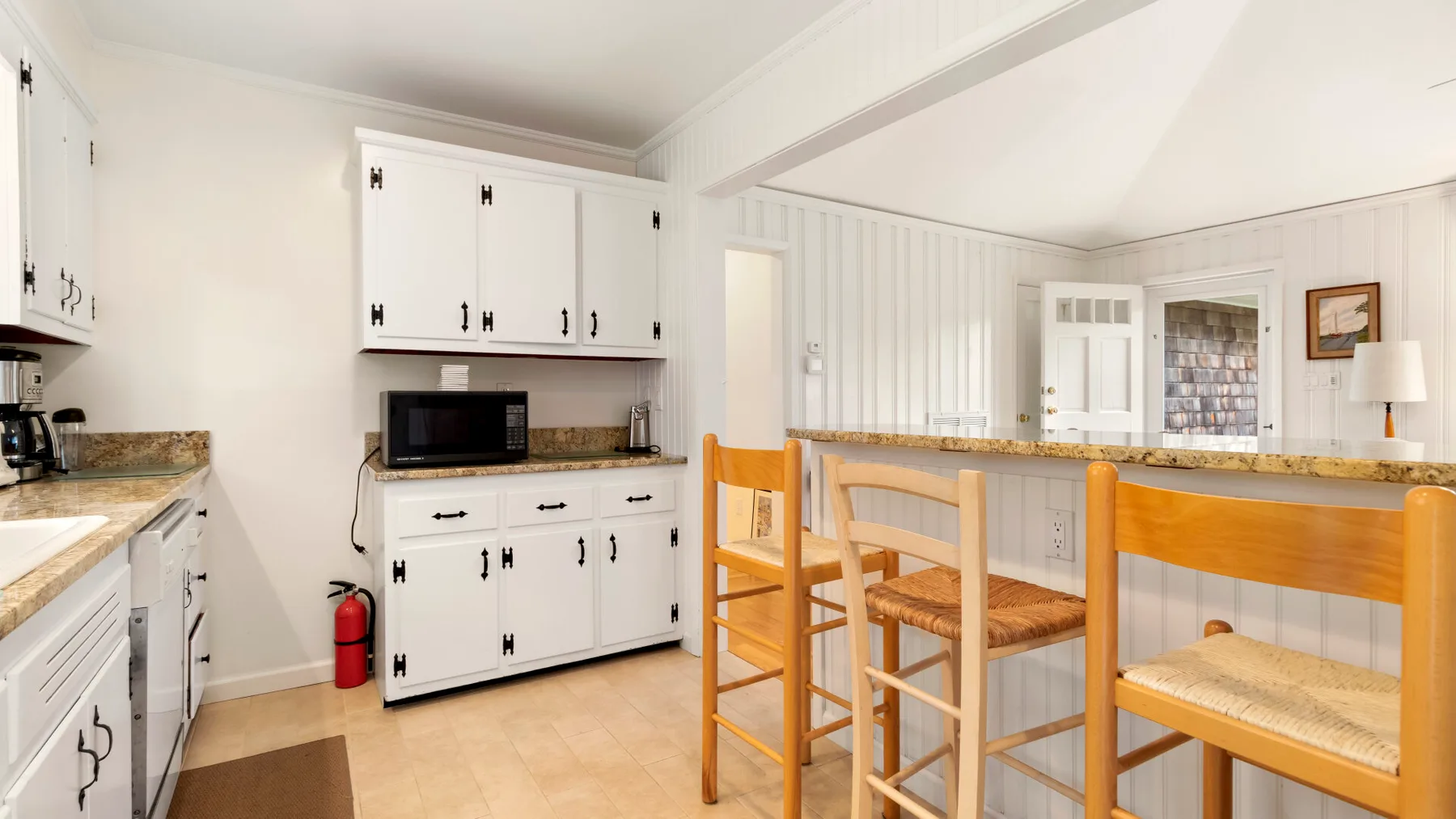Una cocina luminosa con armarios blancos y una barra de madera con asientos.