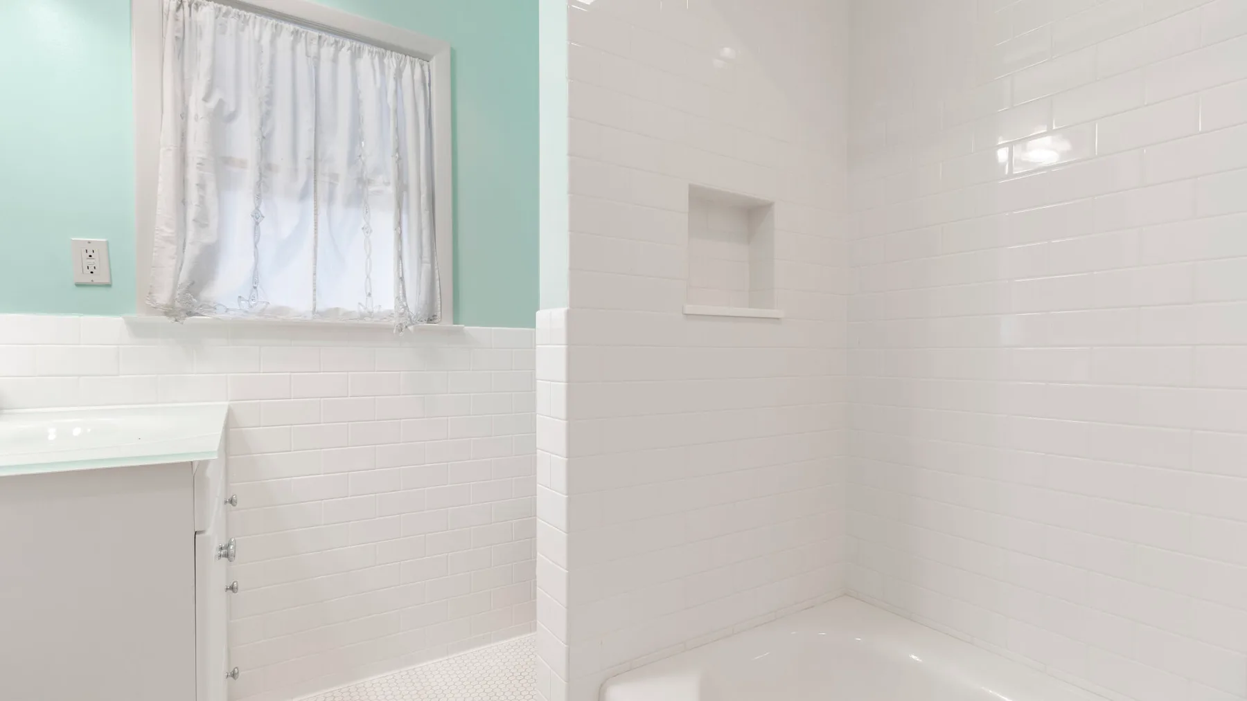 Un baño alicatado con bañera y una ventana con cortina.