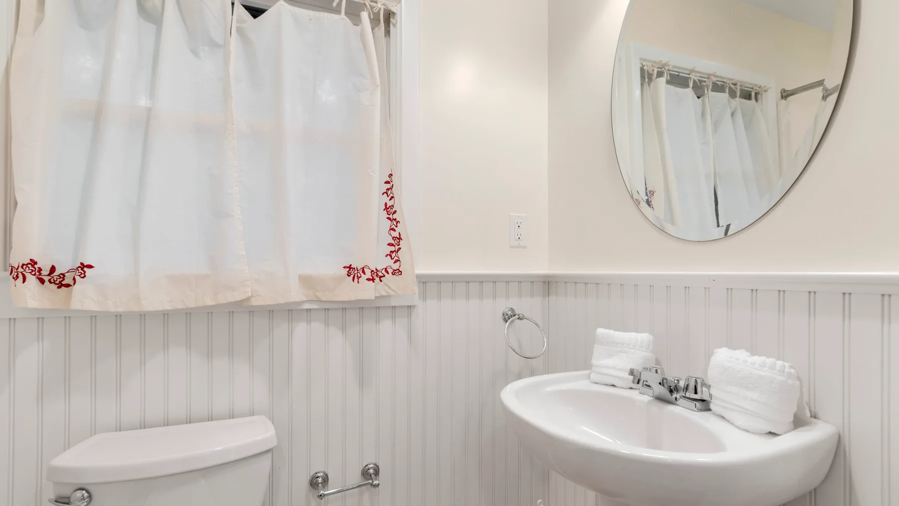 Un baño con lavabo, espejo y cortinas blancas.