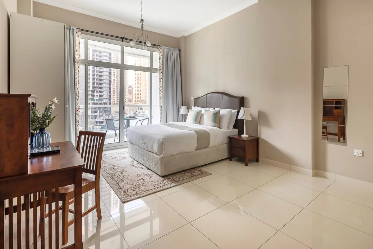 Un dormitorio luminoso con una cama junto a grandes ventanas y una mesa de comedor.